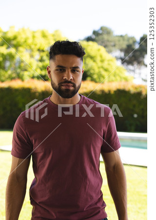 Young man in casual wear standing confidently in sunny backyard garden Young man in casual wear standing confidently in sunny backyard garden 125352303