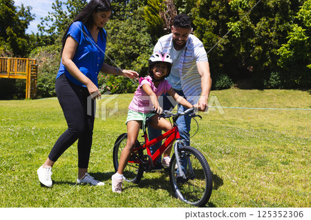 Parents teaching daughter to ride bicycle in park, enjoying sunny day together 125352306