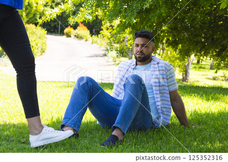 Man sitting on grass in park, looking up at standing person, enjoying nature Man sitting on grass in park, looking up at standing person, enjoying nature 125352316