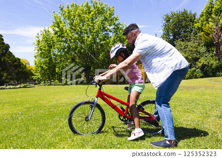 Father teaching daughter to ride bicycle in park, enjoying sunny day together Father teaching daughter to ride bicycle in park, enjoying sunny day together 125352323