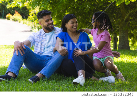 Smiling family sitting on grass in park, enjoying sunny day together 125352345