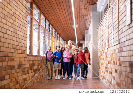 Female teacher with diverse group of students standing in school hallway, smiling 125352912