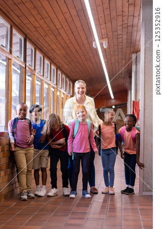 Female teacher with diverse group of school children standing in hallway, smiling together Female teacher with diverse group of school children standing in hallway, smiling together 125352916