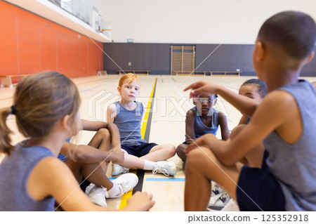 In school gym, diverse children sitting in circle, listening to teammate during discussion In school gym, diverse children sitting in circle, listening to teammate during discussion 125352918
