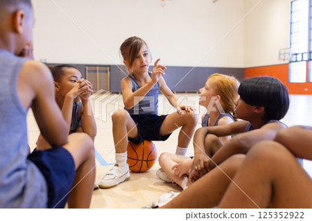 In school gym, diverse children sitting on floor discussing basketball strategy together 125352922