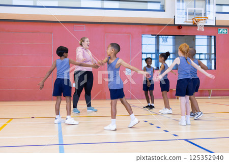 In school gym, diverse children playing game with female teacher, holding hands in circle In school gym, diverse children playing game with female teacher, holding hands in circle 125352940
