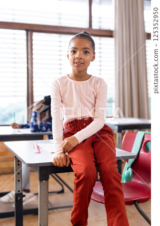In school, girl sitting on desk, smiling confidently in classroom setting 125352950