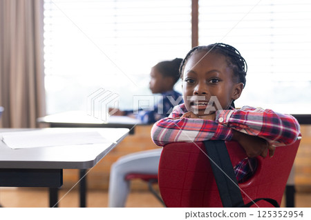 In school, african american girl sitting at desk and smiling, enjoying classroom environment 125352954
