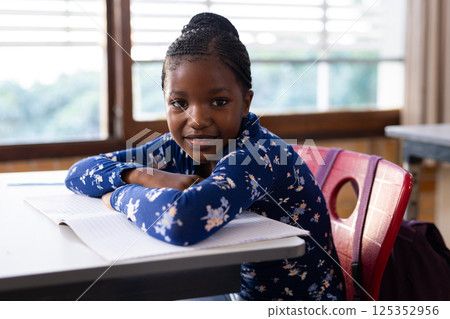 In school, african american girl sitting at desk with open notebook, smiling at camera 125352956