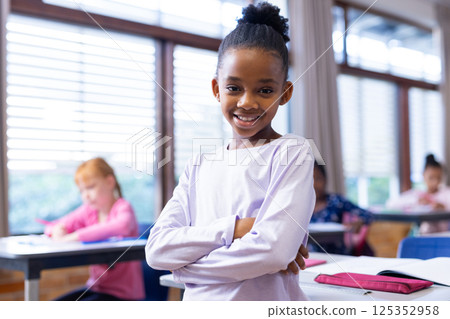 At school,, standing, smiling african american girl in classroom with diverse students in background At school,, standing, smiling african american girl in classroom with diverse students in background 125352958