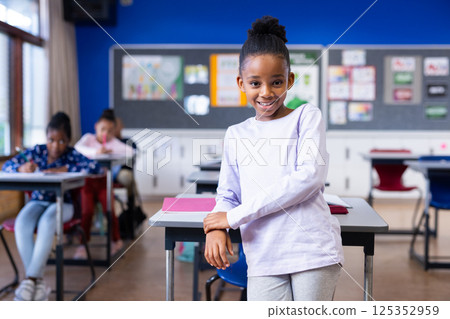 At school, smiling african american girl near desk, diverse classmates studying in background At school, smiling african american girl near desk, diverse classmates studying in background 125352959