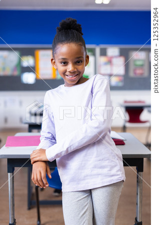 Smiling african american girl standing by desk in classroom, enjoying school environment Smiling african american girl standing by desk in classroom, enjoying school environment 125352964