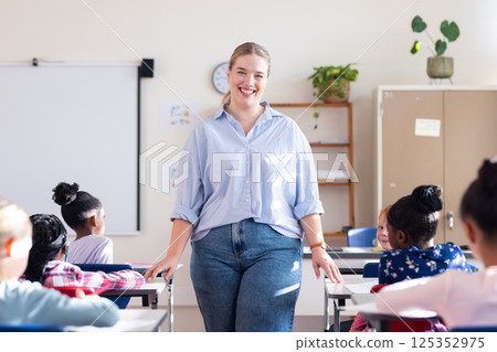 Smiling female teacher standing in classroom with diverse students sitting at desks in school 125352975