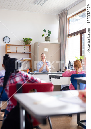 Female teacher clapping hands, engaging diverse students in classroom during school lesson Female teacher clapping hands, engaging diverse students in classroom during school lesson 125352979