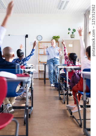 Engaging diverse students in classroom, female teacher raising hands and participating in school 125352982