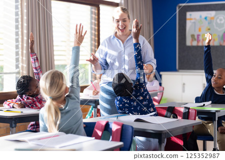 In school, female teacher engaging with diverse students raising hands in classroom discussion In school, female teacher engaging with diverse students raising hands in classroom discussion 125352987