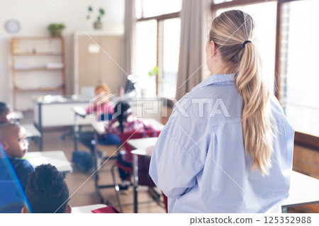 In school, female teacher standing in classroom, diverse students sitting at desks listening In school, female teacher standing in classroom, diverse students sitting at desks listening 125352988