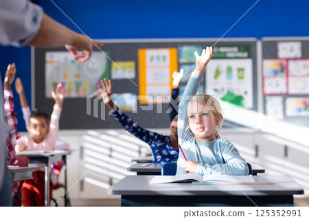 In school, diverse students raising hands in classroom, participating in lesson In school, diverse students raising hands in classroom, participating in lesson 125352991