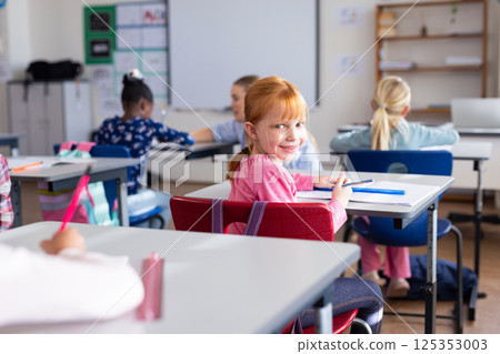 In school, girl smiling and holding pencil while sitting at desk in classroom 125353003