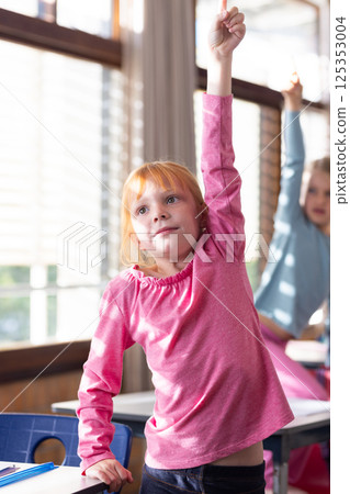 In school, girl raising hand in classroom, eager to answer question 125353004