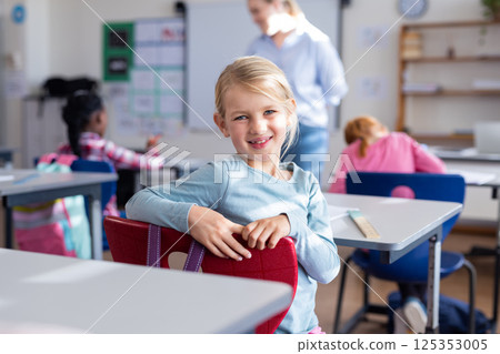 In school, smiling girl sitting at desk in classroom with classmates In school, smiling girl sitting at desk in classroom with classmates 125353005