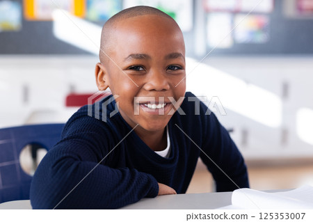 Smiling african american boy sitting at desk in school classroom, looking at camera Smiling african american boy sitting at desk in school classroom, looking at camera 125353007