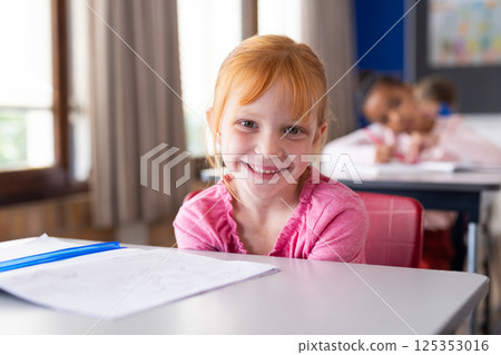 Smiling girl in school classroom sitting at desk with open notebook Smiling girl in school classroom sitting at desk with open notebook 125353016