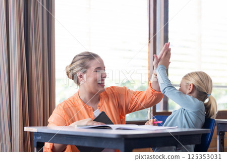 In school, female teacher and girl high-fiving while working at desk 125353031