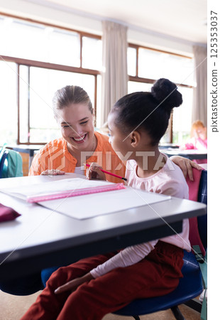 In school, female teacher smiling while helping young girl with writing assignment In school, female teacher smiling while helping young girl with writing assignment 125353037