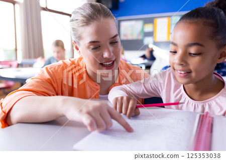 At school, Female teacher helping girl with homework in classroom, focusing on learning together At school, Female teacher helping girl with homework in classroom, focusing on learning together 125353038