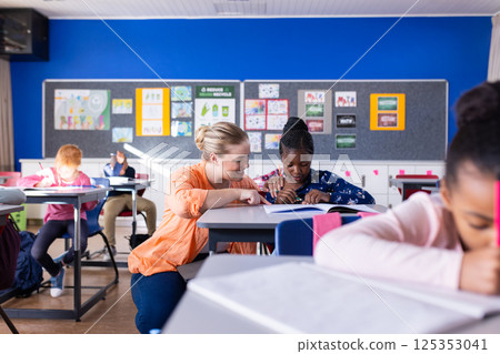 In school, female teacher helping african american girl with assignment in classroom, smiling 125353041