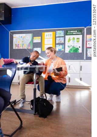 In school, female teacher helping african american boy with classwork at desk, smiling together 125353047