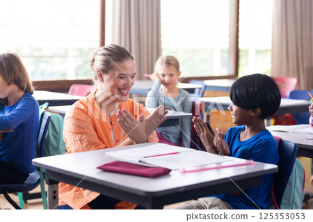 Female teacher and boy clapping hands together in school classroom, smiling and engaged 125353053