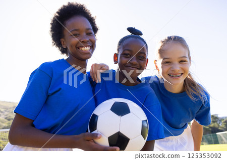 Smiling school diverse girls holding soccer ball, enjoying outdoor sports activity together 125353092