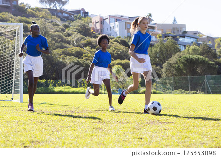 Playing soccer on school field, diverse girls in sports uniforms running with ball Playing soccer on school field, diverse girls in sports uniforms running with ball 125353098
