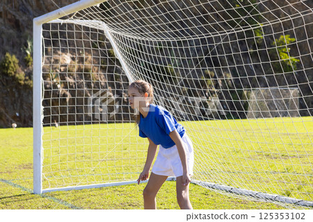 Playing soccer, girl in blue jersey standing as goalkeeper on school field 125353102