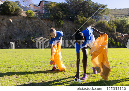 Picking up trash, diverse girls in school uniforms cleaning up field together Picking up trash, diverse girls in school uniforms cleaning up field together 125353110