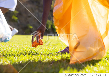 Picking up trash, african american girl in school uniform cleaning up grassy field Picking up trash, african american girl in school uniform cleaning up grassy field 125353111