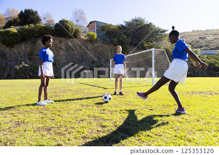 Playing soccer on school field, three diverse girls practicing with soccer ball Playing soccer on school field, three diverse girls practicing with soccer ball 125353120