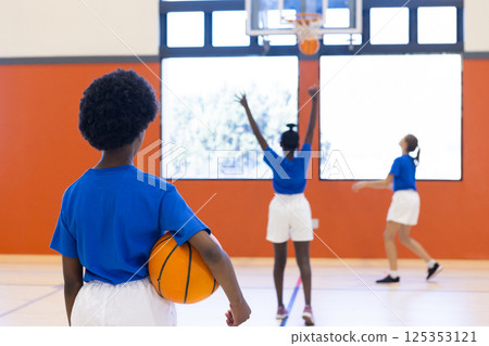 Playing basketball in school gym, diverse girls practicing shooting and holding ball 125353121