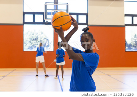Playing basketball in school gym, african american girl holding ball and smiling at camera 125353126
