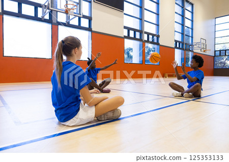 Playing basketball in school gym, diverse girls passing ball and having fun 125353133
