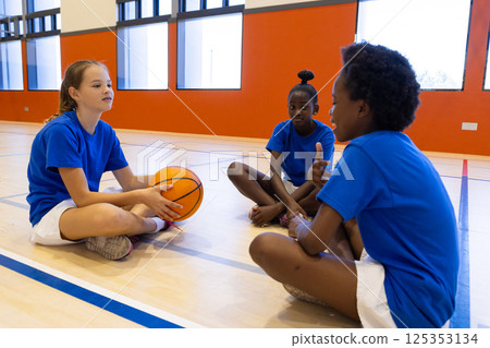 Sitting on gym floor, diverse girls in school discussing basketball game strategy 125353134