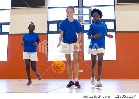 Playing basketball in school gym, three diverse girls dribbling and running together Playing basketball in school gym, three diverse girls dribbling and running together 125353137