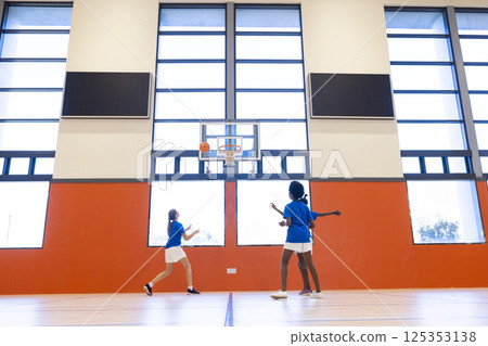 Playing basketball in school gym, diverse girls shooting hoops and practicing teamwork Playing basketball in school gym, diverse girls shooting hoops and practicing teamwork 125353138