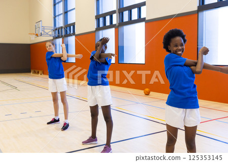 In school gym, three diverse girls stretching arms during physical education class 125353145