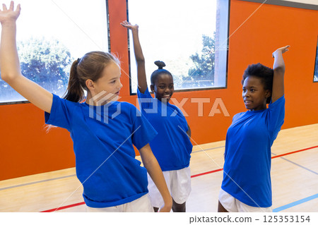 In school gym, diverse girls practicing dance routine, wearing blue shirts and white shorts In school gym, diverse girls practicing dance routine, wearing blue shirts and white shorts 125353154