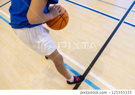 Playing basketball in school gym, girl dribbling ball on court Playing basketball in school gym, girl dribbling ball on court 125353155