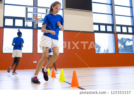 Running through cones, girl participating in school gym class activity 125353157
