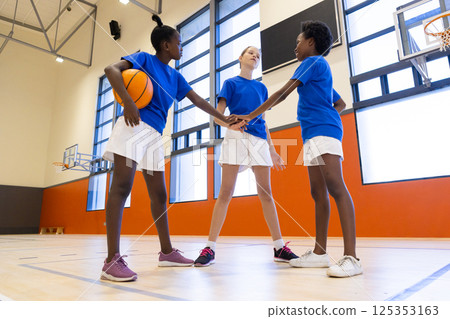 Playing basketball, three school diverse girls in gym holding hands in huddle 125353163